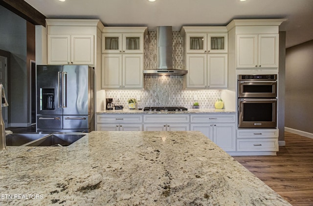 kitchen featuring backsplash, wall chimney range hood, appliances with stainless steel finishes, wood finished floors, and cream cabinetry