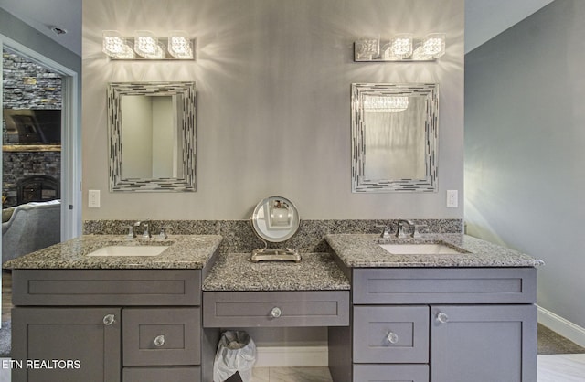 full bathroom with a sink, baseboards, two vanities, and a stone fireplace