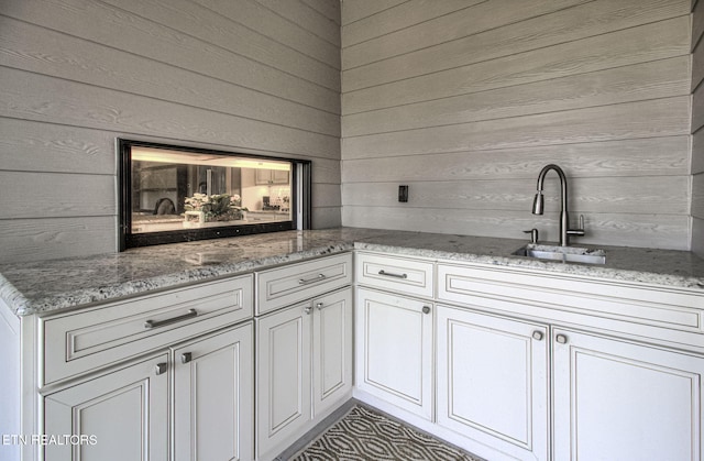 kitchen with light stone counters, white cabinets, wood walls, and a sink