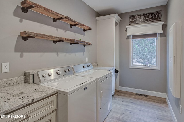 clothes washing area with visible vents, baseboards, washer and dryer, light wood-style floors, and cabinet space