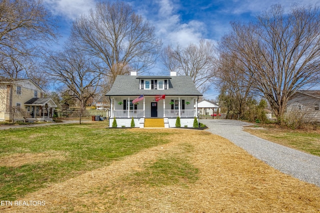 view of front of property featuring driveway, a porch, a front yard, a shingled roof, and a chimney