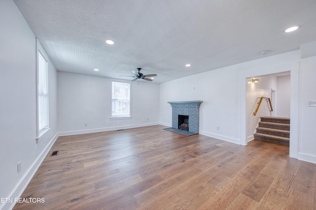 unfurnished living room with visible vents, a brick fireplace, stairway, wood finished floors, and a textured ceiling