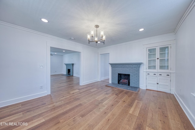 unfurnished living room with crown molding, a fireplace, light wood-type flooring, and a chandelier