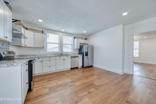 kitchen featuring light stone countertops, appliances with stainless steel finishes, light wood-style floors, white cabinets, and a sink