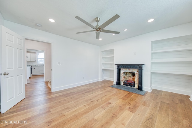 unfurnished living room with baseboards, a textured ceiling, a fireplace, and light wood finished floors