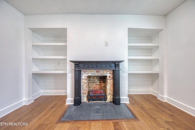 interior details with a fireplace with flush hearth, wood finished floors, baseboards, and built in features