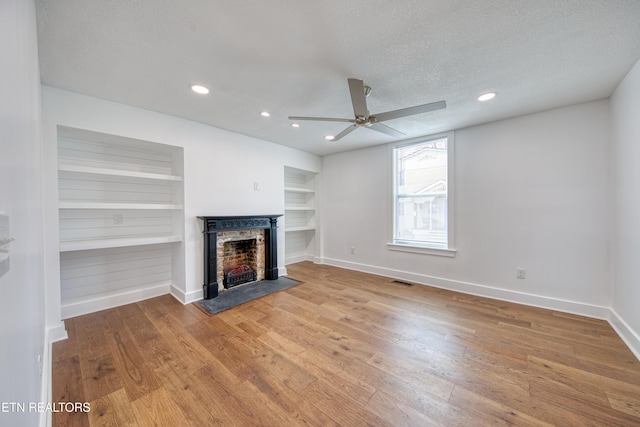 unfurnished living room featuring a fireplace with flush hearth, wood finished floors, baseboards, and a textured ceiling