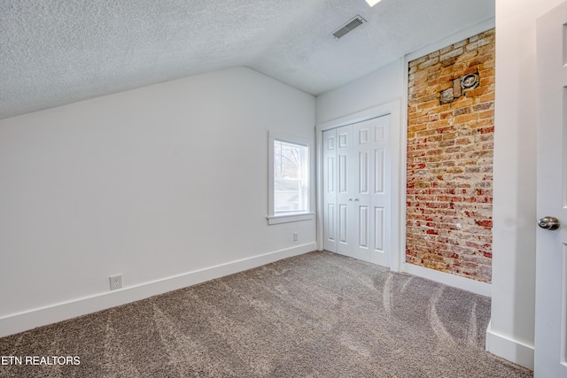 unfurnished bedroom featuring baseboards, visible vents, carpet floors, vaulted ceiling, and a textured ceiling