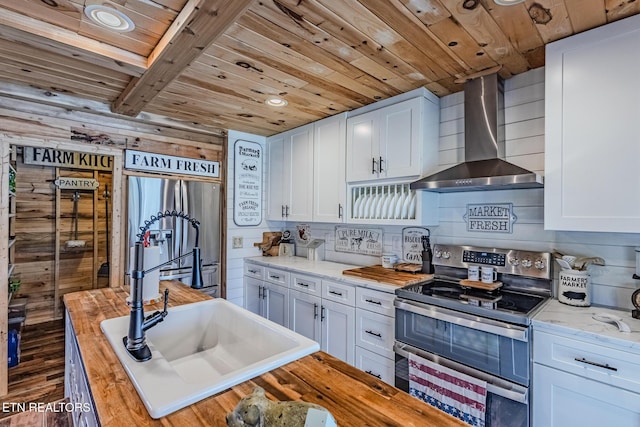 kitchen featuring wood counters, stainless steel appliances, white cabinets, wooden ceiling, and wall chimney range hood