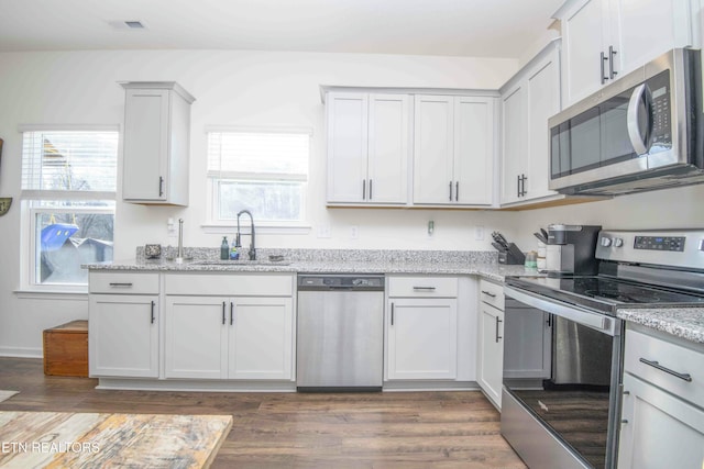 kitchen with a sink, light stone counters, appliances with stainless steel finishes, and dark wood-style floors