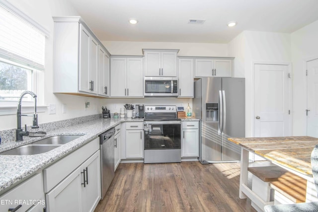 kitchen featuring visible vents, a sink, light stone counters, stainless steel appliances, and dark wood-style flooring