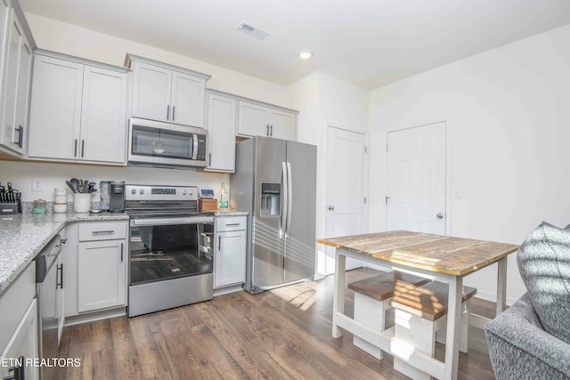 kitchen featuring dark wood-type flooring, light stone countertops, visible vents, and stainless steel appliances