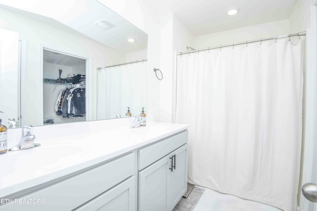 full bath with double vanity, visible vents, a walk in closet, and a sink