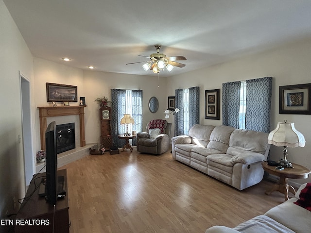 living room with a glass covered fireplace, recessed lighting, wood finished floors, and a ceiling fan