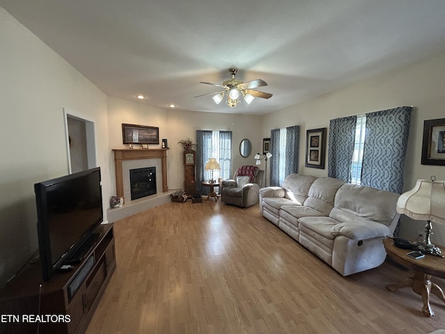 living room featuring a glass covered fireplace, wood finished floors, and ceiling fan