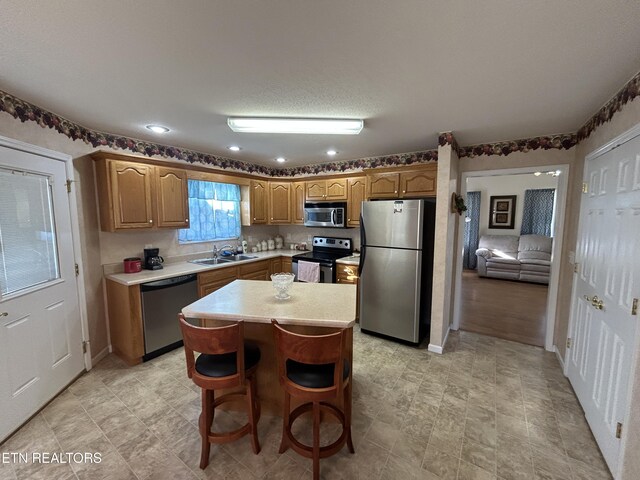 kitchen with brown cabinets, a sink, a kitchen island, appliances with stainless steel finishes, and light countertops