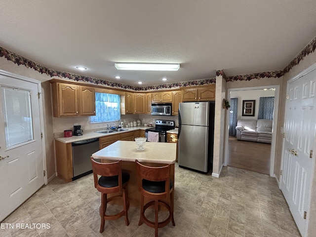 kitchen featuring a kitchen island, a sink, light countertops, appliances with stainless steel finishes, and brown cabinets