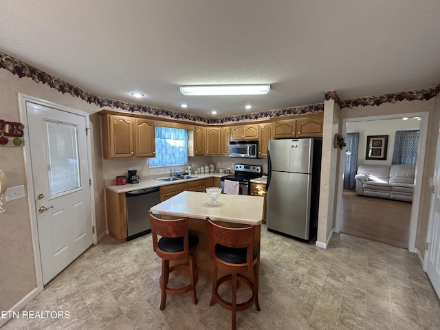 kitchen featuring brown cabinetry, a kitchen island, a sink, stainless steel appliances, and light countertops