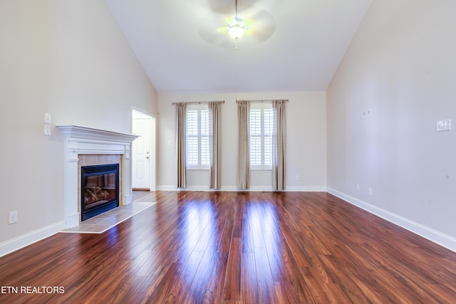 unfurnished living room with wood finished floors, baseboards, high vaulted ceiling, ceiling fan, and a tile fireplace