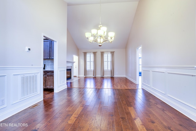 unfurnished living room with an inviting chandelier, a fireplace with flush hearth, dark wood-style floors, and visible vents