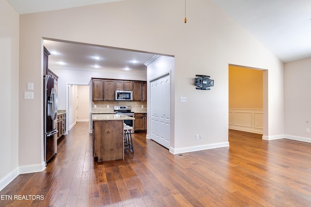 kitchen with backsplash, a breakfast bar, vaulted ceiling, appliances with stainless steel finishes, and dark wood-style flooring