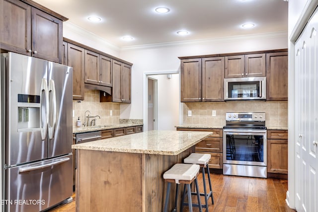 kitchen featuring ornamental molding, a sink, a kitchen island, appliances with stainless steel finishes, and dark wood-style flooring