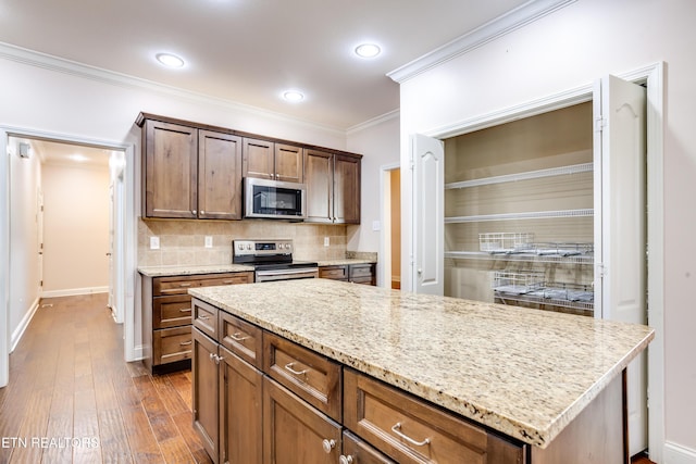 kitchen featuring ornamental molding, light stone counters, decorative backsplash, appliances with stainless steel finishes, and dark wood-style floors