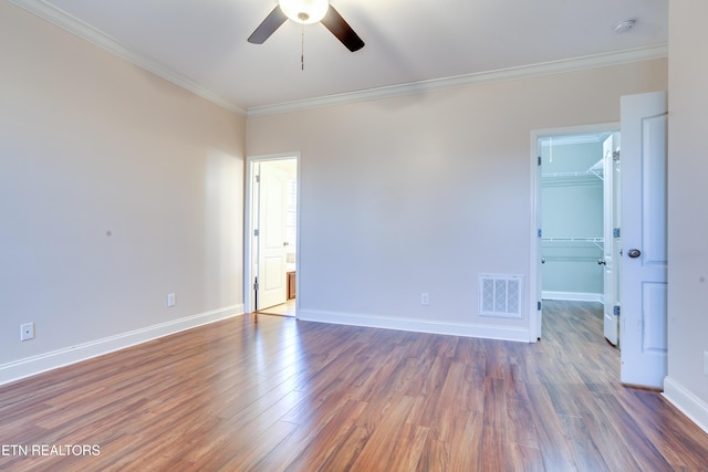 empty room with visible vents, baseboards, wood finished floors, and ornamental molding