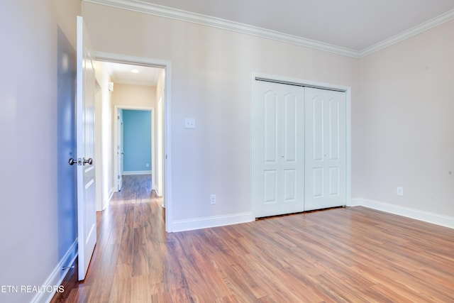 unfurnished bedroom featuring crown molding, wood finished floors, baseboards, and a closet