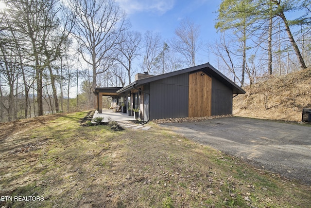 view of property exterior featuring driveway, a chimney, and a patio