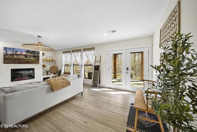 living room with a glass covered fireplace, french doors, visible vents, and light wood finished floors