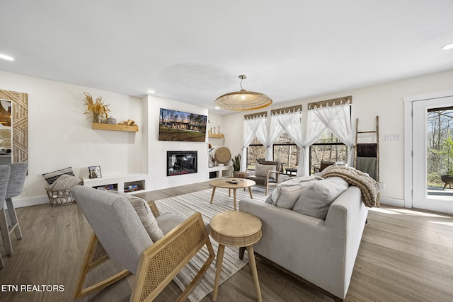 living area with a glass covered fireplace, wood finished floors, and recessed lighting