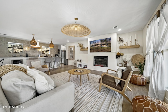 living area featuring a glass covered fireplace, recessed lighting, wood finished floors, and visible vents