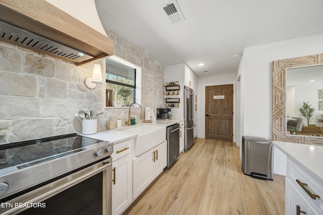 kitchen featuring light wood finished floors, visible vents, white cabinets, stainless steel appliances, and wall chimney exhaust hood