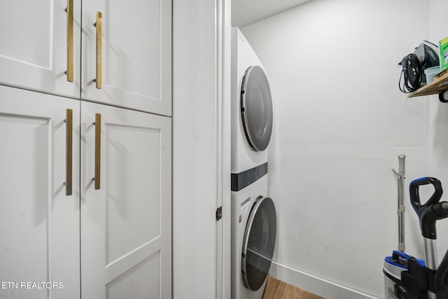 laundry room featuring cabinet space, stacked washer and clothes dryer, and wood finished floors