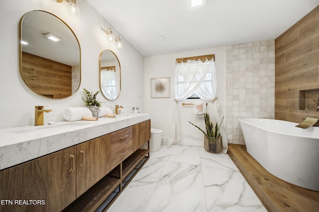 full bathroom with double vanity, a freestanding bath, a sink, toilet, and marble finish floor