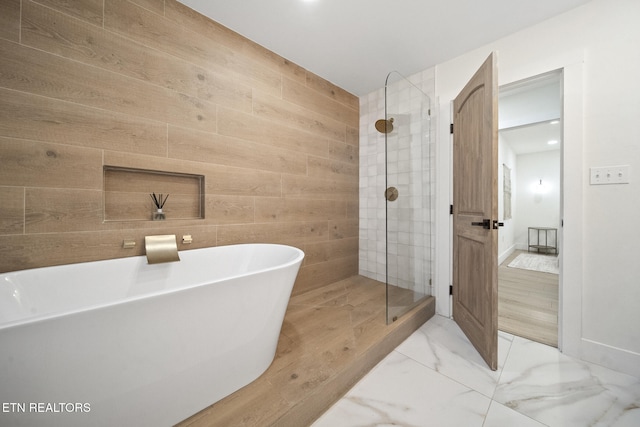 full bathroom featuring wooden walls, marble finish floor, a stall shower, and a freestanding bath