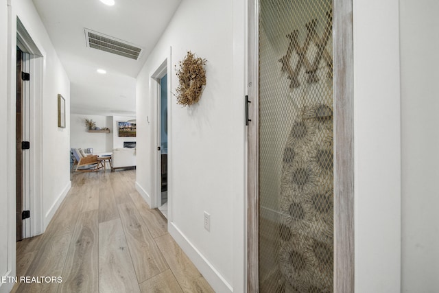 hallway featuring light wood-style flooring, baseboards, and visible vents