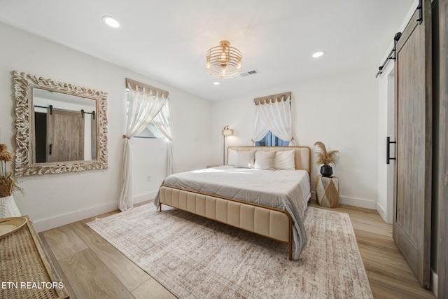 bedroom with a barn door, baseboards, visible vents, and light wood finished floors