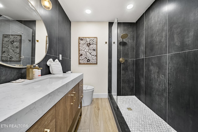 bathroom with baseboards, toilet, a tile shower, wood finished floors, and vanity