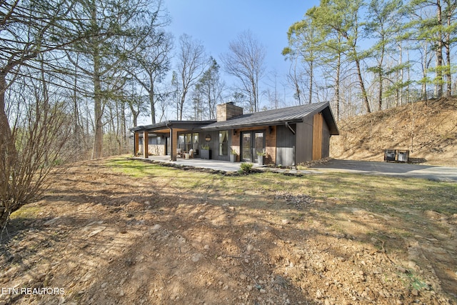 back of house with metal roof, driveway, and a chimney