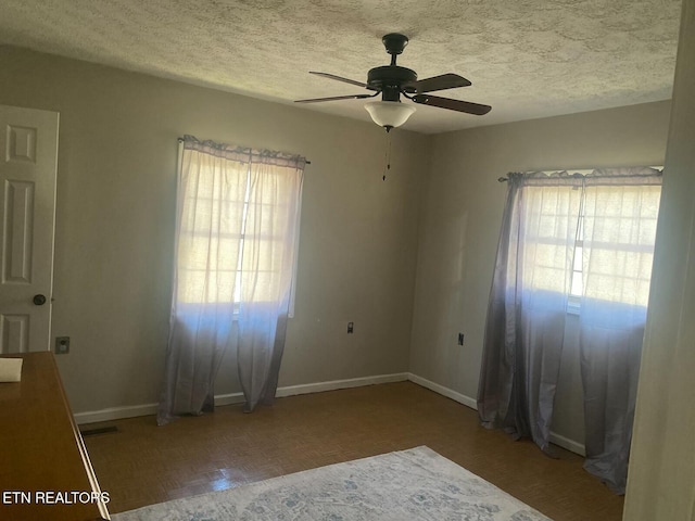 unfurnished room with visible vents, a textured ceiling, baseboards, and a ceiling fan