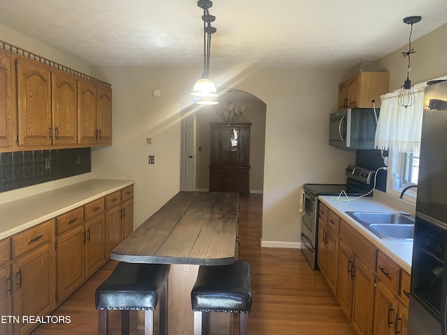 kitchen featuring arched walkways, brown cabinets, appliances with stainless steel finishes, and wood finished floors