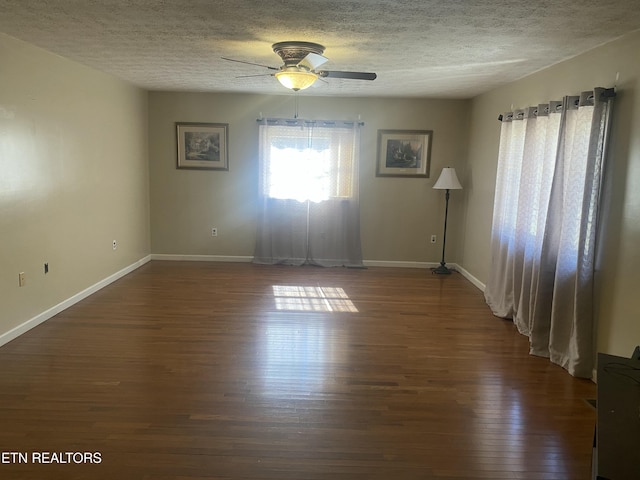 empty room with ceiling fan, dark wood-type flooring, baseboards, and a textured ceiling