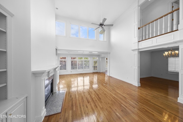 unfurnished living room with baseboards, a high ceiling, a fireplace, ceiling fan with notable chandelier, and wood-type flooring
