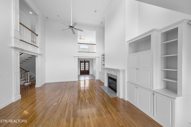 unfurnished living room with a high ceiling, a ceiling fan, a fireplace, stairway, and light wood-style flooring