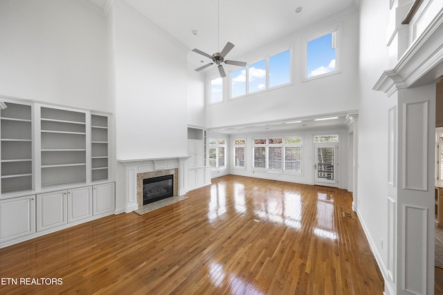 unfurnished living room featuring ceiling fan, ornamental molding, a high ceiling, a premium fireplace, and wood-type flooring