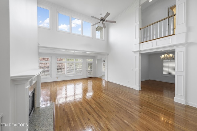 unfurnished living room with baseboards, a high ceiling, a tiled fireplace, wood finished floors, and ceiling fan with notable chandelier