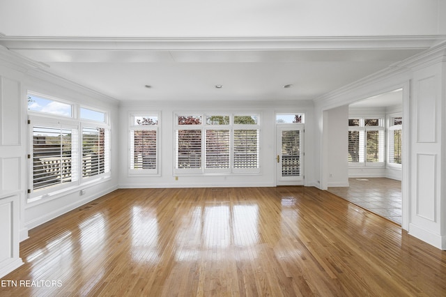 unfurnished living room featuring light wood-style flooring, ornamental molding, and a wealth of natural light