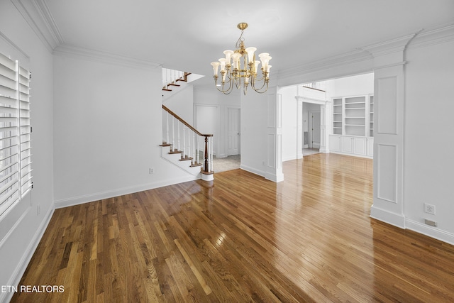 unfurnished dining area with a notable chandelier, ornamental molding, stairs, built in shelves, and wood finished floors